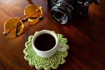 Xícara com café, câmera antiga e óculos com lentes amarelas sobre uma mesa de madeira.