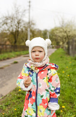 a little girl in a bright jacket stands outside in the spring and holds a branch with spring white flowers in her hands