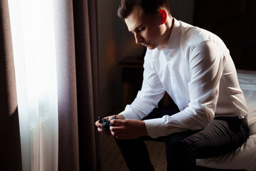 young man in a white shirt sitting on the bed and holding a bow tie