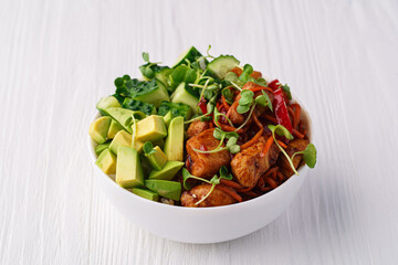 Bowl with rice, chicken, avocado, cucumber, carrot, bell pepper and pea sprouts on a white wooden background
