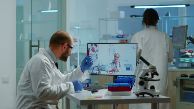 Male chemist listening professional doctor on video call, discussing during virtual meeting in medical research laboratory. Scientist examining vaccine evolution using high tech researching treatment