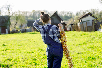 Happy Teenager girl in summer yellow boxing field. Girl farmer preparing for planting bulbs. Bouquet of onions in the hands. Sunny warm day in the village