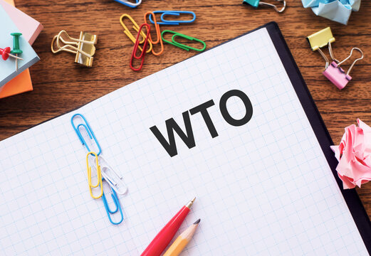 Notebook With Text WTO (World Trade Organization) On A Table With Colored Paper Clips And Wrinkled Sheets.