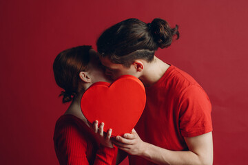 Man and woman young couple kissing and hiding behind heart-shaped box