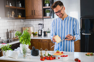 Young chef grating cheese over freshly home made tomato and basil pasta