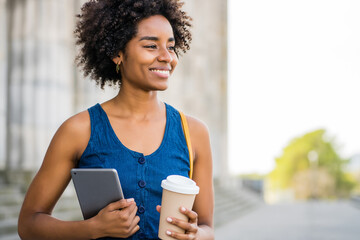 Business woman holding digital tablet and coffee outdoors.