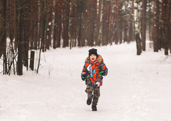 Little boy runs through the snow in winter in the woods. Happy childhood