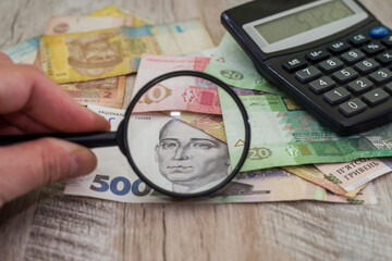 A hand with a magnifying glass checks the hryvnia.