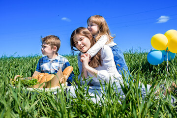 Three happy kids sitting on picnic on the field. blue sky, green grass. bread, pies and fruits in a basket.