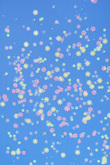Fototapeta na wymiar Festive blue background with colorful flowers. Multi-colored small artificial flowers. Flat lay, top view.