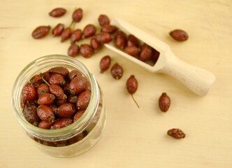 Rose hips, dried wild rose fruits on jar, wooden spoon, natural wooden background, super food, healthy fruits, vitamin C and antioxidants resource