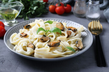 Tagliatelle pasta with mussels and basil on a plate on gray background. Close up