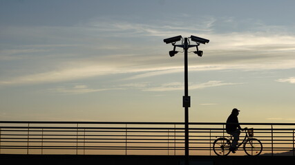 Obraz premium silhouette of cyclist walking down security camera street at sunset