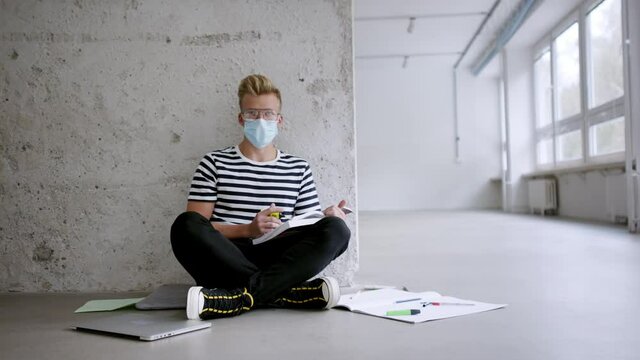 Young student with face mask sitting on floor back at college or university, coronavirus concept.