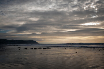 a long reflective beach with a row of stones leading into the sea