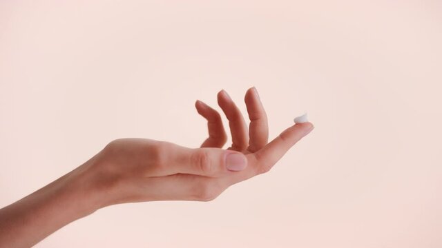 Close-up shot of a female hand with a drop of beauty cream on the top of the finger against beige background