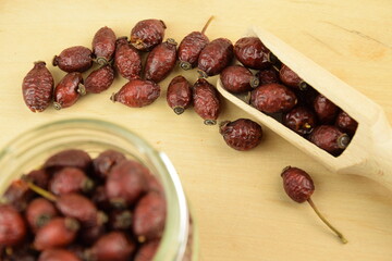 Rose hips, dried wild rose fruits on wooden spoon and jar, natural wooden background, super food, healthy fruits, vitamin C and antioxidants resource