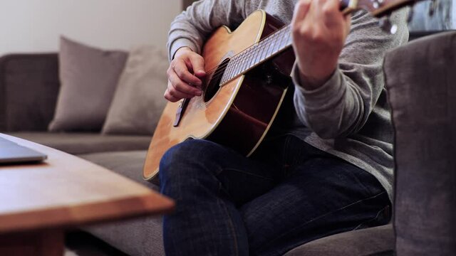 家のソファに座ってギターを練習する日本人の男性