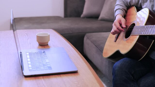 家のソファに座ってギターを練習する日本人の男性