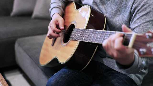 家のソファに座ってギターを練習する日本人の男性