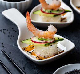 Close up of a homemade sushi roll with cucumber, radish and a prawn in a small white dish.
