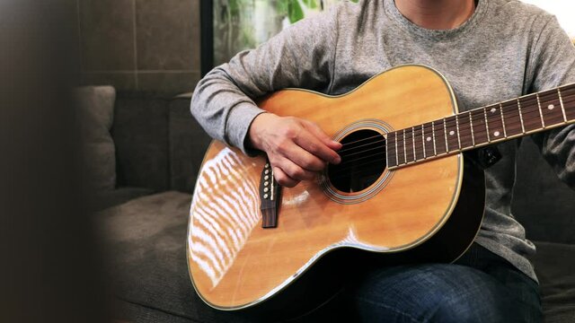 家のソファに座ってギターを練習する日本人の男性