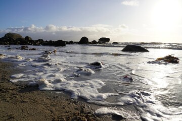 Foamy wave at the beach at sunset with rocks and sand
