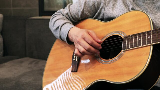 家のソファに座ってギターを練習する日本人の男性