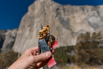 Close-up of hand holding healthy energy bar with mountain in background.