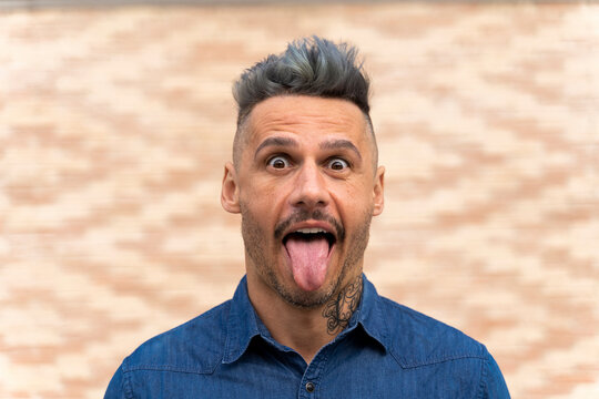 Playful man sticking out tongue against wall