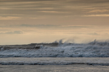 waves crashing into the wind creating spray flying over the top of them