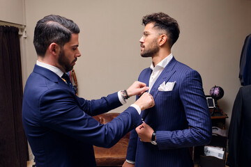 Tailor in his menswear store adjusting customers blue pinstripe suit