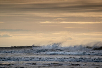 waves crashing into the wind creating spray flying over the top of them