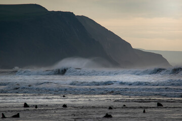 waves crashing into the wind creating spray flying over the top of them