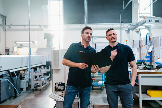 Male technicians with file document discussing at factory