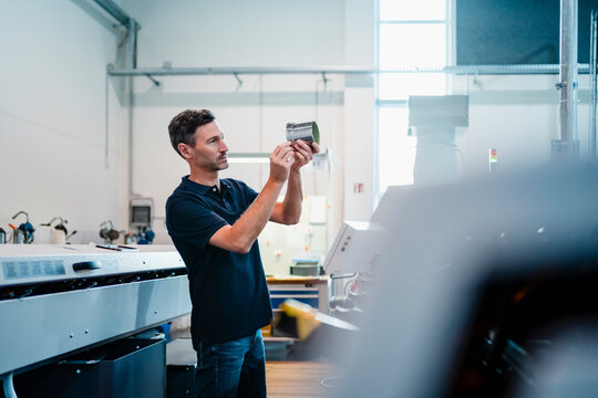 Male engineer with analyzing machine part in factory