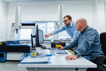 Male engineers working on computer while standing at office