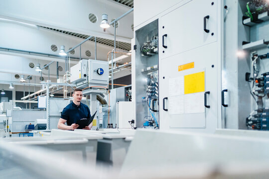 Male technician with file document surrounded by machines in factory