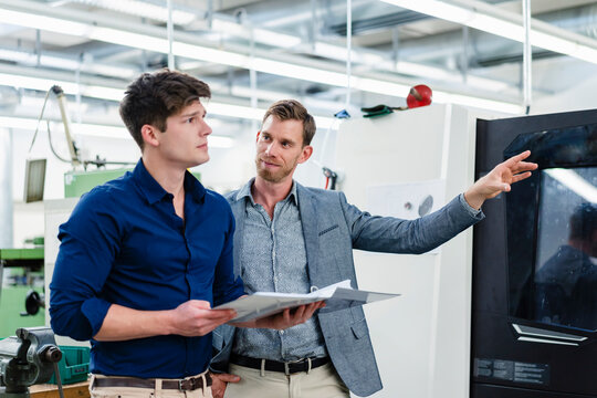 Male entrepreneur looking at colleague while discussing about machinery equipment in industry