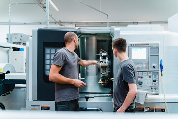 Engineer showing machine part to trainee while working at industry