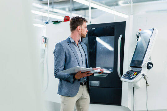 Male entrepreneur holding file document while looking at machinery equipment in industry