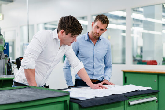Male entrepreneur looking at engineer while working on floor plan in industry