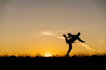 Silhouette of man practicing martial arts against setting sun