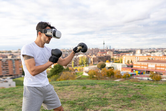 Male acrobat wearing virtual reality headset practicing boxing on hill in city