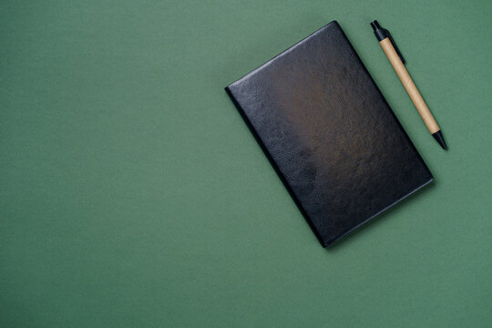 Black leather notebook on a paper green background, notepad mock up, top view shot