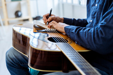 Male composer writing in note pad while sitting at studio