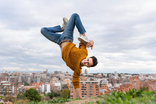 Flexible young man doing handstand on hill in city against sky