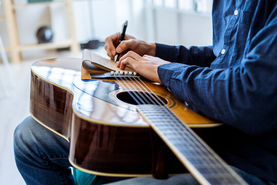 Male composer writing in note pad while sitting at studio