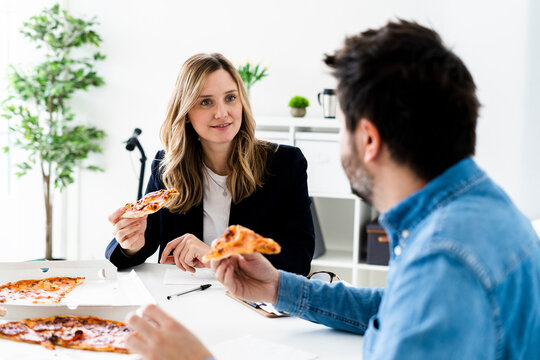 Business people eating pizza and talking in office during break