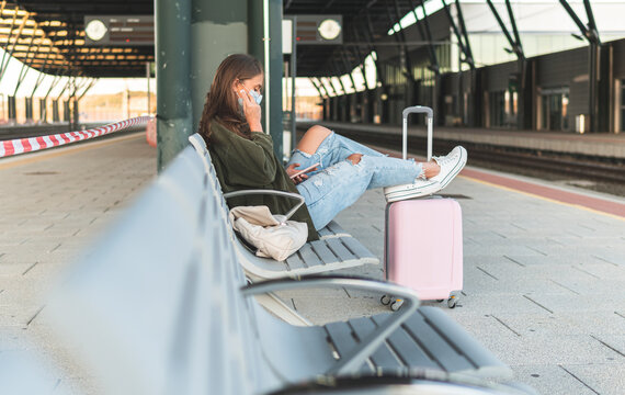 Young woman wearing mask using mobile phone while sitting on chair at railroad platform